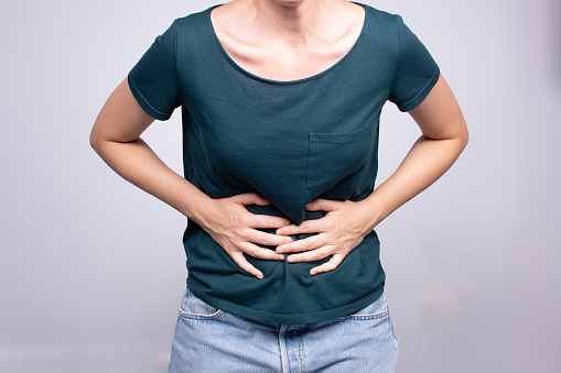 A woman gripping her abdomen in discomfort, depicting symptoms that may indicate health issues or abdominal pain