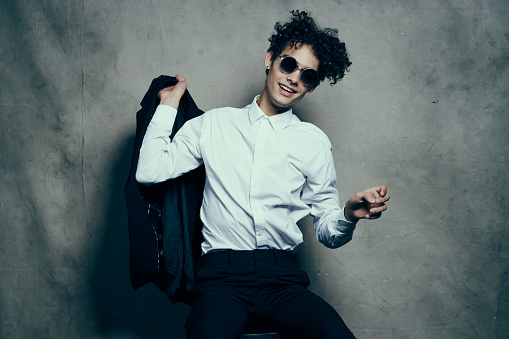 stylish guy in a suit sits on a chair indoors and glasses on his face. High quality photo