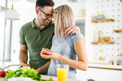 Happy couple in love talking while preparing a meal in the kitchen.