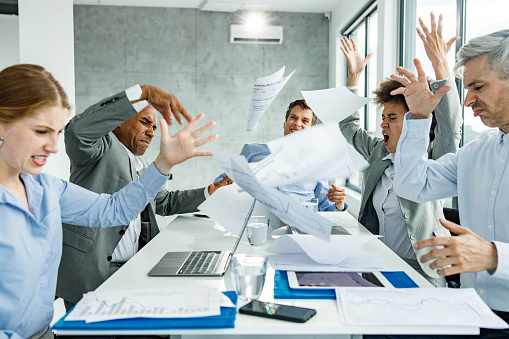 Group of frustrated business colleagues feeling displeased while throwing paperwork during a meeting in the office.