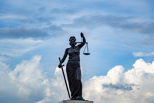 Sculpture of Lady Justice or Themis symbol of justice and law, Femida outdoors against blue cloudy sky background copy space cut out
