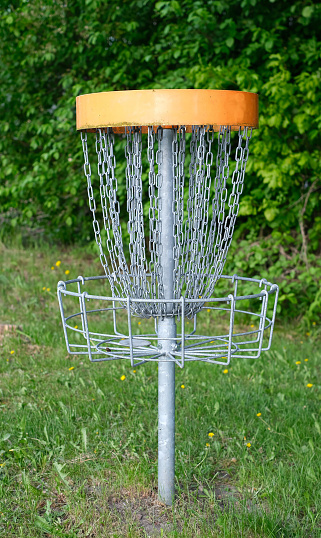 A disc golf basket with chains sits on a grassy field, surrounded by trees.