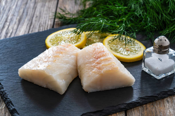 istock Fresh raw codfish fillet with lemon and dill on black stony cutting board on wooden table 2082925786