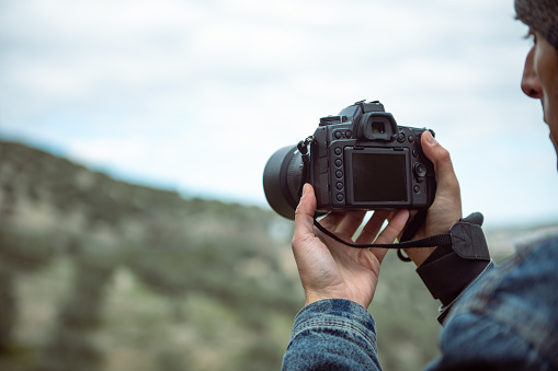 Details on the digital camera in the hands of male photographer capturing the beauty of nature, photographing mountains. Travel photographer taking picture on his professional camera. Copy ad space.