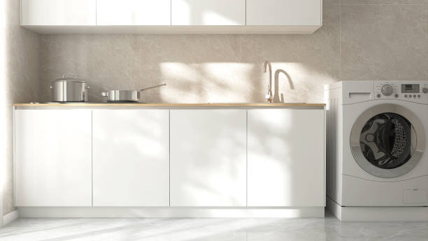 istock Kitchen cabinet counter with sink, induction stove, cupboard, washing machine in sunlight on beige marble tile wall in background 2082936480
