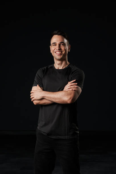 istock In his striking black ensemble, the beautiful young man stands with folded arms, emitting an aura of confidence and charm. 2082943850