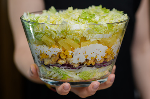 Layered salad with turkey, corn, Chinese cabbage and pineapple in a glass bowl