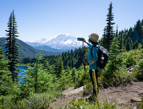 Woman taking photos of snow-capped Mount Rainier using smartphone. Summit Lake Trail. Mt Rainier National Park. Washington State.