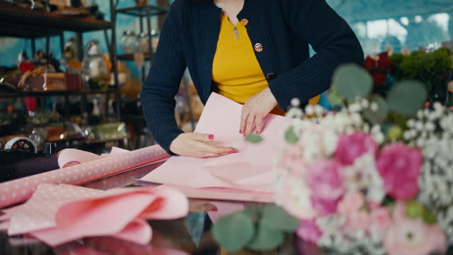 Mature Female Florist Preparing Pink Paper for Wrapping the Bouquet at Table in Shop