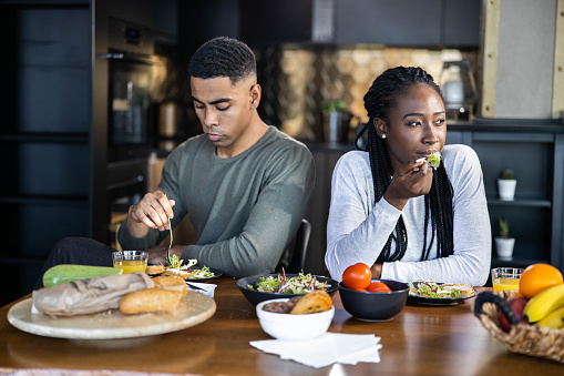Young black couple having problems in their relationship while ignoring each other during lunch at dining table.