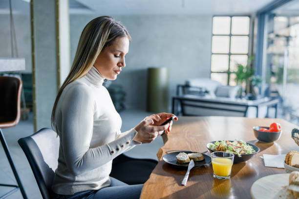 istock Young woman using cell phone during her meal at home. 2083000871