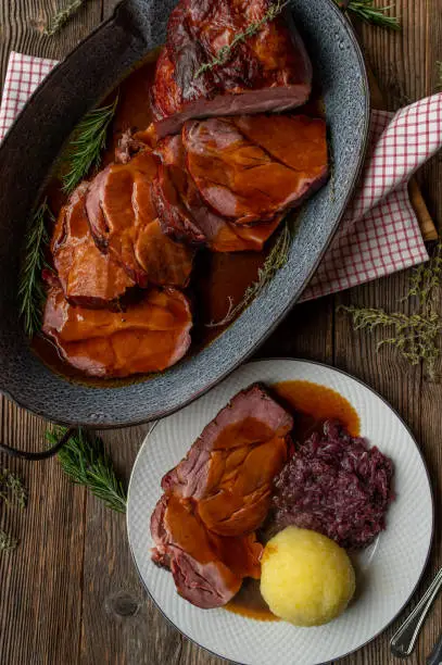 German pork roast with delicious brown sauce. Traditional and rustic cuisine. Served ready to eat in a roasting pan on wooden table background.
