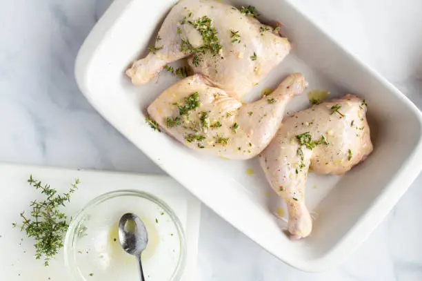 Marinated raw and uncooked chicken legs or thighs with herbs, olive oil and garlic in a casserole dish on light background. top view with copy space