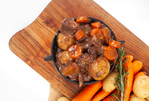 Traditional South African pot (potjie). Stew cooked in cast iron pot over open flames.
 Top view of beef potjie on wooden chopping board on white wit copy space