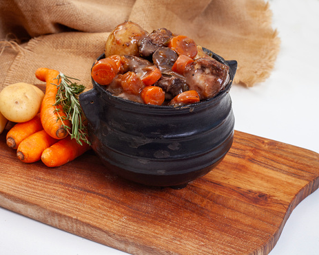 Traditional South African pot (potjie). Stew cooked in cast iron pot over open flames.
Beef potjie on wooden board with burlap, on white with copy space