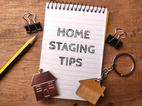 House keychain and notebook with the word HOME STAGING TIPS on wooden background