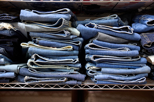 A large number of jeans stacked on a rack.