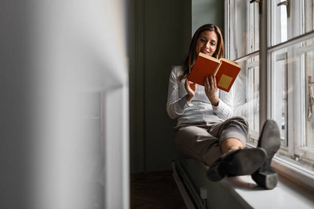 istock Businesswoman Finding Solace on Window Ledge with Book 2083029150