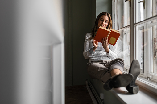 Businesswoman on Window Ledge Reading Book
