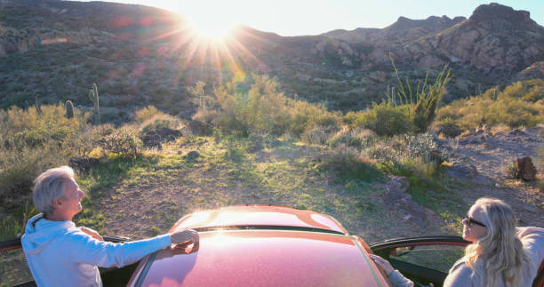 Mature couple watch sunset over mountains by vehicle in desert