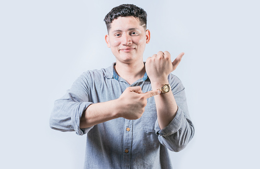 Smiling young man pointing at his wrist watch isolated. Portrait of person pointing his wrist watch on isolated background