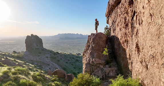Hiker stands on rock pinnacle above desert at sunset