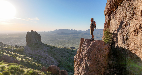 Hiker stands on rock pinnacle above desert at sunset