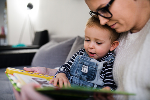 mom read book with son and sit on sofa at home
