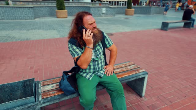 Elderly bearded man sits on a bench and talks on the phone