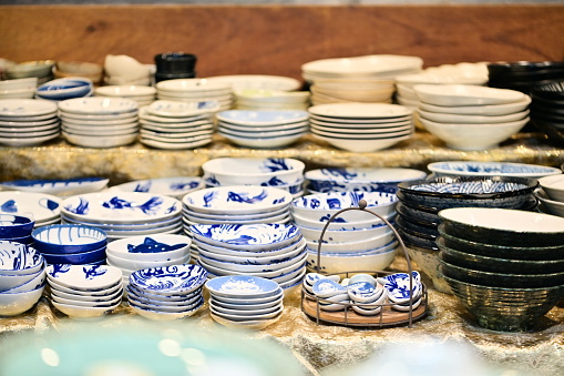 A close-up of various plates, bowls, and accessories at a market stall, showing the intricate details and patterns on the tableware.