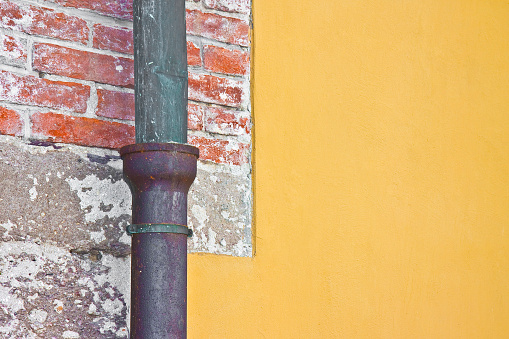 Old rusty copper and cast iron downpipe against a brick and yellow plaster wall - image with copy space.