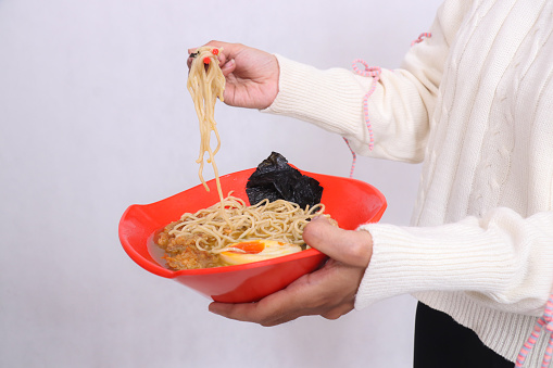 hands of indonesia woman in hijab carrying bowl of delicious ramen (chinese food) and picking up noodles with chopsticks for advertising, food and culinary content