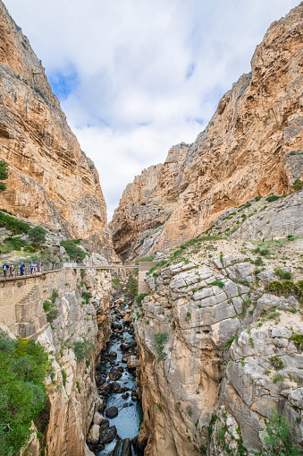 People walking on the Caminito del Rey, a long walkway hanging over 100 metres up on a sheer cliff face in a narrow gorge that runs through cliffs, canyons, and a large valley