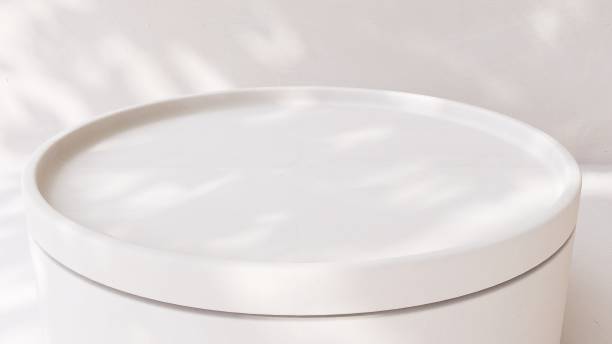 istock Empty round matte white stone table podium in dappled sunlight, leaf foliage shadow on white concrete wall 2083183135