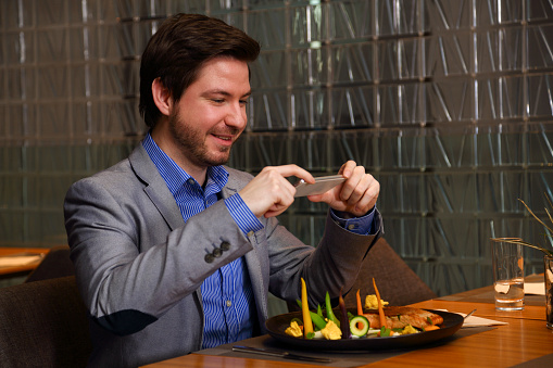 Young man in luxury restaurant photographing his food. Art plate.
