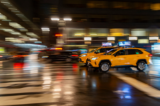Street photography near Grand Central Station, New York City.  This is on a very wet and dark spring night with wet roads creating reflections of two yellow cabs at a cross roads.  Slow shutter speed creates movement blur for surrounding area.