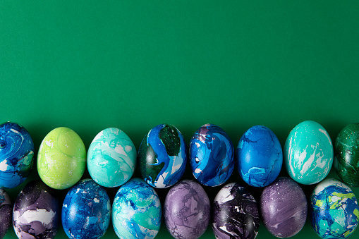 Close-up of 12 eggs dyed blue, pink, red, yellow, orange, and green on a gray weathered wooden background