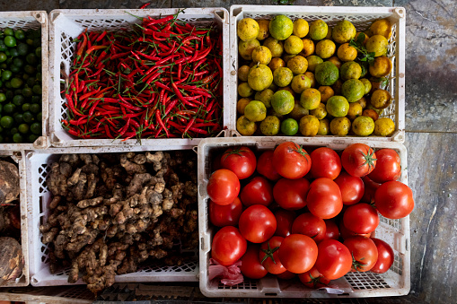 Overhead view of baskets of fresh red chile peppers, lemons, ginger root and ripe tomatoes at a produce market in Vietnam.