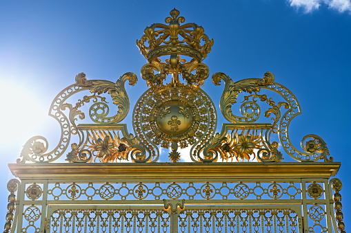 Versailles, Paris, France, June 30, 2022. Gorgeous detail of the golden gate of the royal palace. The late afternoon light enhances its brilliance.