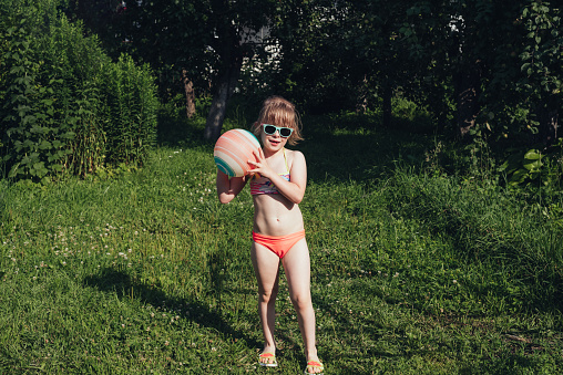 Child girl in a swimsuit plays with an inflatable ball. Childhood, leisure on weekends and holidays