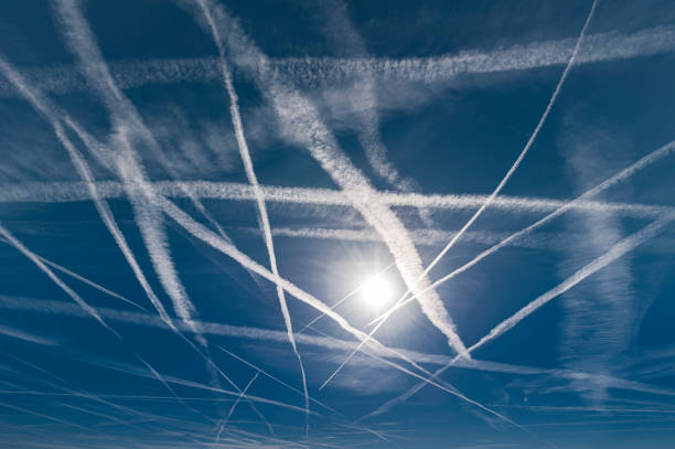 Fresh and partly already dissolving vapor trails in the blue sky with the bright sun