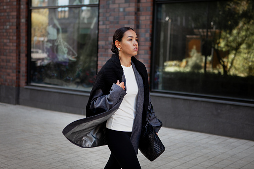 Stylish fashion woman strolls down the street in multilayer clothes oversized blazer, black leggings. Fashionable outfit, street style.