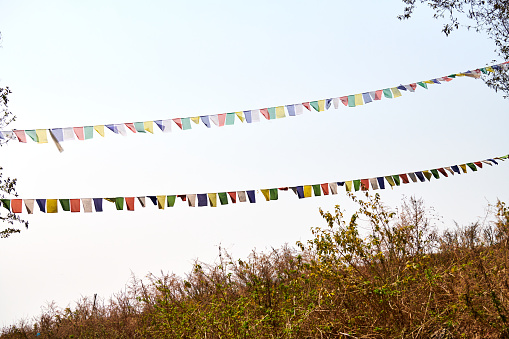 Colorful Tibetan prayer flags flutter ancient prayers into serene mountain wind at top of high hill on blue sky background, symbolizing spiritual energy peaceful tranquility