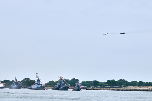 Military fighter jets are flying over Russian naval forces parade warships along coastline, seafaring tradition of military ships formation at Navy Day, nautical spectacle of russian sea power