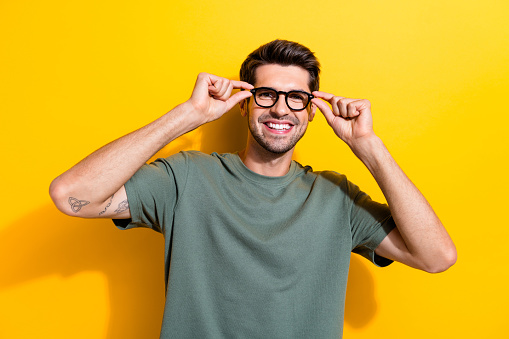 Portrait of intelligent positive guy wear stylish t-shirt fingers touching glasses at checkup isolated on vivid yellow color background.