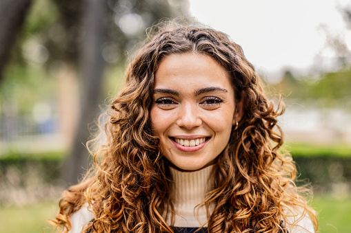 A woman with stunning curly hair beams with a captivating smile in nature.