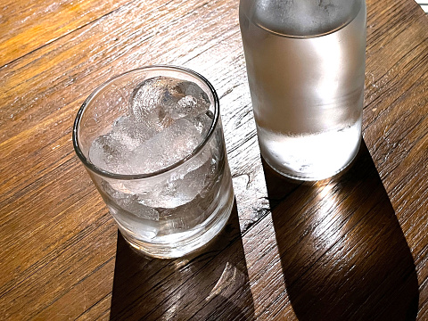 Selective focus, A clear glass filled with ice and clear glass bottle holds cold mineral water sits on wooden table, water use to quench thirst