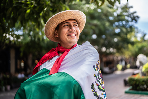 Dancer young man holding Mexican flag and contemplating outdoors