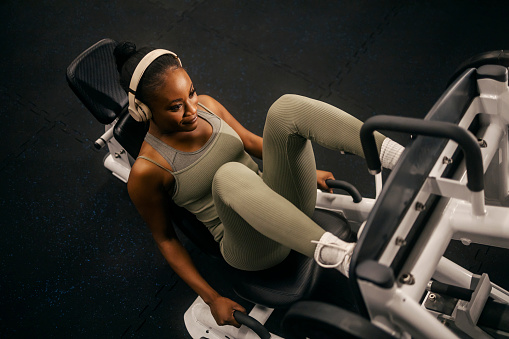 From above view of a strong female athlete practicing legs on a leg press machine at the gym.