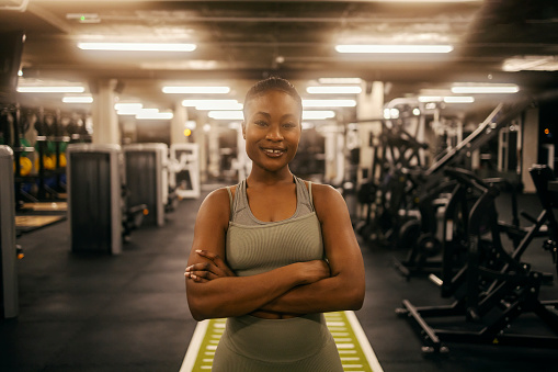 A female black athlete is standing in a gym with arms crossed and smiling at the camera.